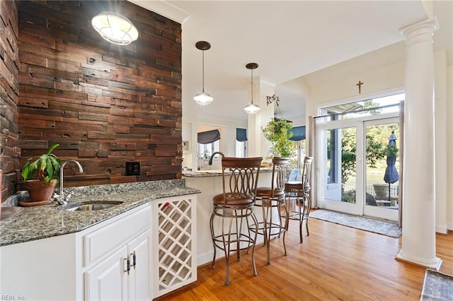 kitchen featuring ornate columns, light wood-style flooring, light stone counters, and a sink