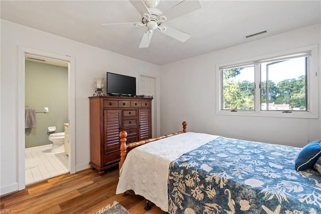 bedroom featuring visible vents, baseboards, a ceiling fan, ensuite bath, and wood finished floors