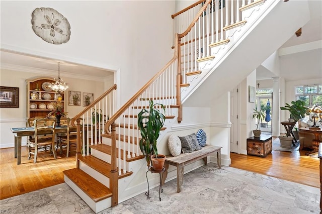 stairs with a towering ceiling, crown molding, a chandelier, and wood finished floors