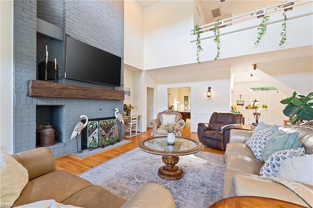 living area with a high ceiling, a fireplace, wood finished floors, and visible vents