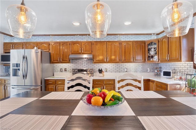 kitchen featuring under cabinet range hood, appliances with stainless steel finishes, brown cabinets, and pendant lighting