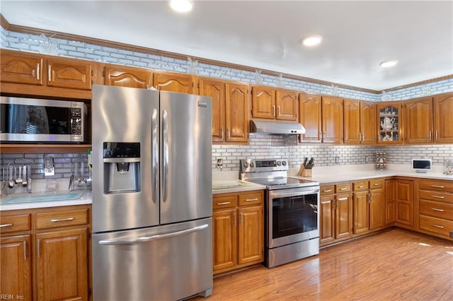 kitchen with under cabinet range hood, light wood-style flooring, stainless steel appliances, and brown cabinetry