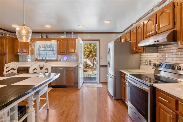 kitchen featuring under cabinet range hood, stainless steel appliances, light countertops, and brown cabinetry