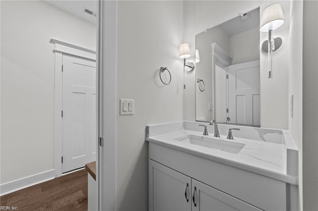 bathroom with visible vents, vanity, baseboards, and wood finished floors