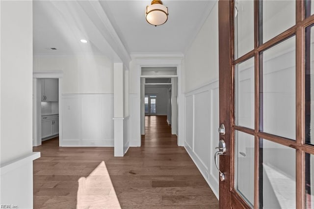 hall with ornamental molding, wainscoting, wood finished floors, and a decorative wall