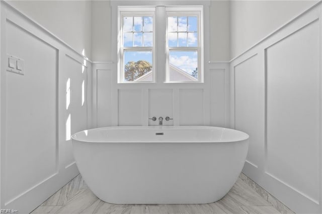 bathroom featuring a freestanding tub, marble finish floor, and a decorative wall