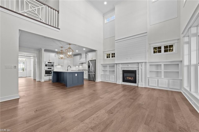 unfurnished living room featuring baseboards, a glass covered fireplace, wood finished floors, a sink, and a notable chandelier