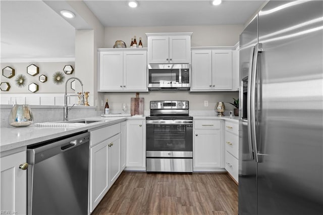 kitchen featuring appliances with stainless steel finishes, white cabinetry, a sink, and wood finished floors