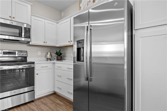 kitchen with white cabinets, appliances with stainless steel finishes, light countertops, and wood finished floors