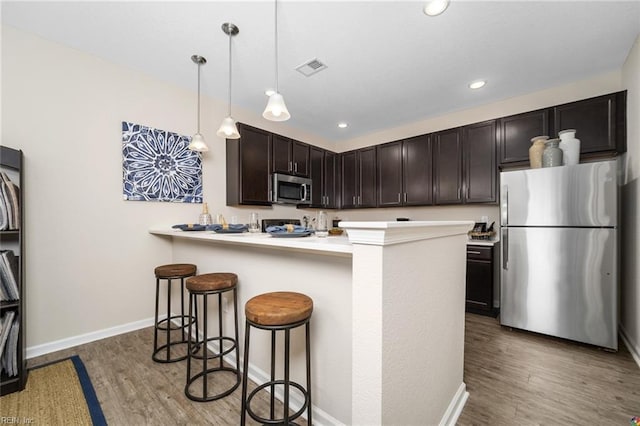 kitchen with light countertops, appliances with stainless steel finishes, light wood-type flooring, and a kitchen bar