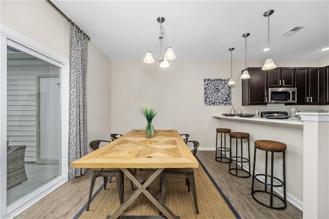 dining room with a chandelier, light wood-style flooring, visible vents, and baseboards