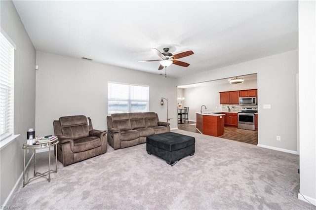 carpeted living area with baseboards, a sink, visible vents, and a ceiling fan