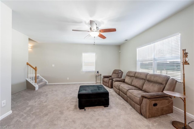 living area with carpet floors, stairway, baseboards, and a ceiling fan