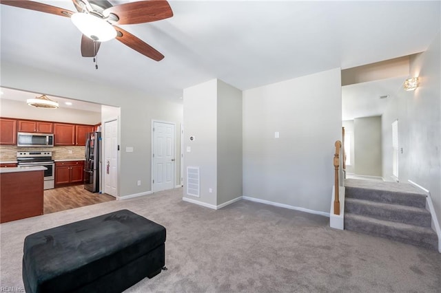 interior space with light colored carpet, a ceiling fan, baseboards, stairs, and visible vents