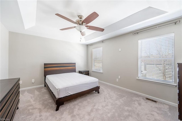 bedroom with light colored carpet, visible vents, baseboards, multiple windows, and a tray ceiling