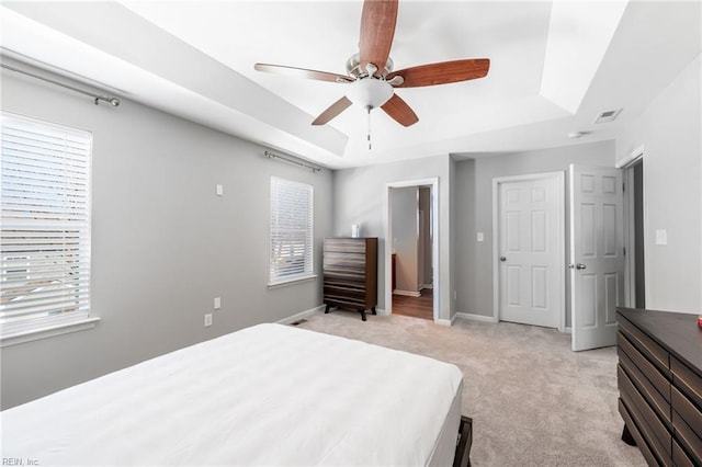 bedroom with multiple windows, baseboards, a raised ceiling, and light colored carpet