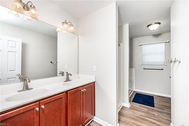 full bath featuring double vanity, wood finished floors, a sink, and baseboards