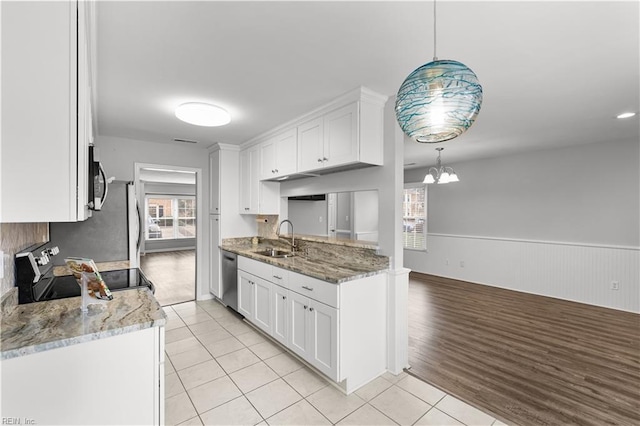 kitchen featuring white cabinets, a wainscoted wall, appliances with stainless steel finishes, a chandelier, and a sink