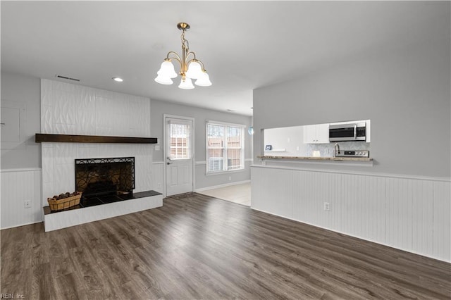 unfurnished living room featuring a fireplace with raised hearth, a notable chandelier, wood finished floors, visible vents, and wainscoting