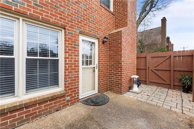 doorway to property featuring brick siding, a patio area, fence, and a gate