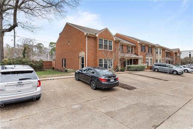 view of front of home with uncovered parking, brick siding, and fence