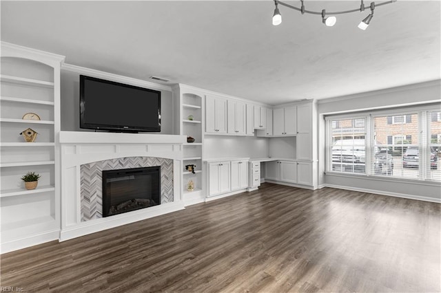 unfurnished living room with dark wood-type flooring, a tile fireplace, built in features, and baseboards