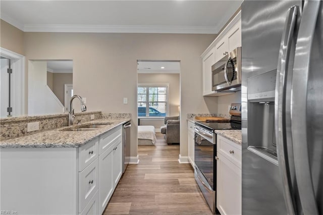 kitchen with light wood finished floors, stainless steel appliances, ornamental molding, white cabinets, and a sink