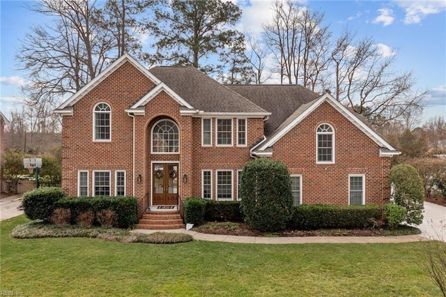 colonial house with a shingled roof, a front yard, french doors, and brick siding