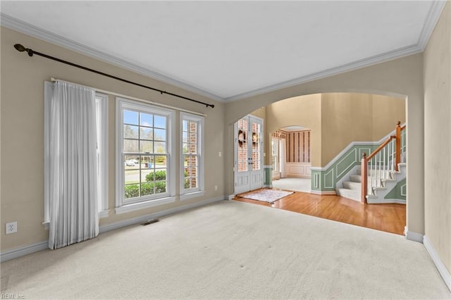 carpeted spare room with arched walkways, visible vents, baseboards, stairway, and crown molding