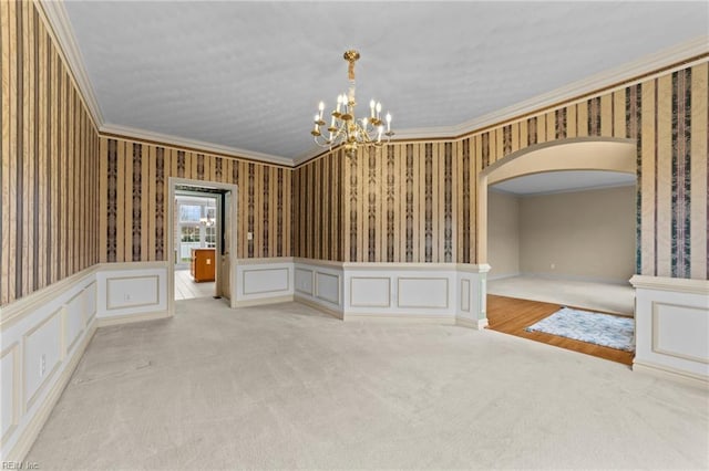 empty room featuring arched walkways, ornamental molding, a decorative wall, and wallpapered walls