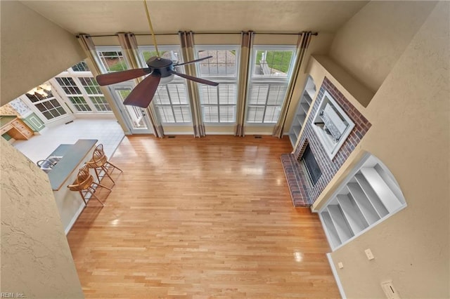 unfurnished living room with ceiling fan, a fireplace, wood finished floors, and a textured wall