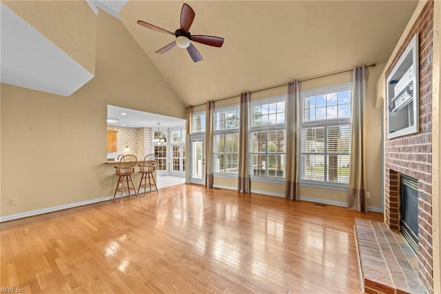 unfurnished living room with high vaulted ceiling, light wood-type flooring, a brick fireplace, and ceiling fan