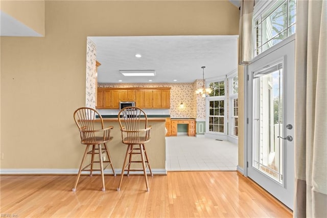 kitchen featuring a notable chandelier, light wood-style floors, brown cabinetry, a peninsula, and a kitchen bar