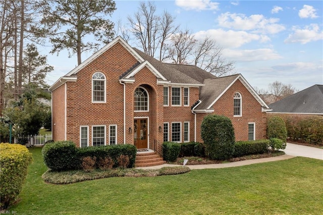 colonial house with a front yard, concrete driveway, brick siding, and fence