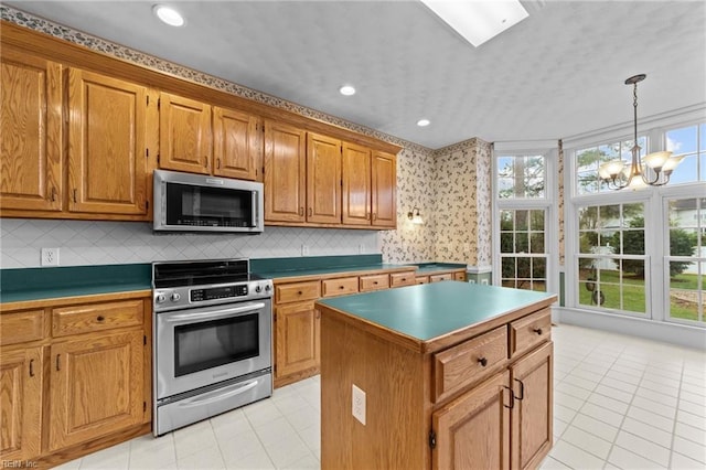 kitchen with a chandelier, light tile patterned flooring, a kitchen island, appliances with stainless steel finishes, and brown cabinets