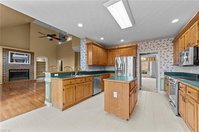 kitchen featuring a center island, appliances with stainless steel finishes, open floor plan, a sink, and wallpapered walls