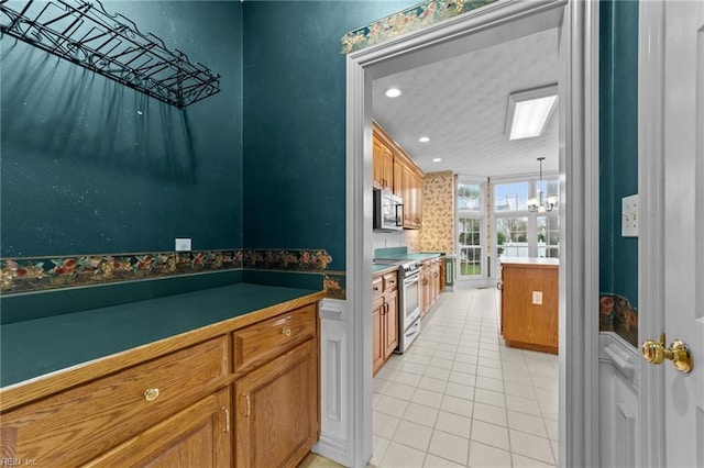 kitchen with light tile patterned floors, appliances with stainless steel finishes, brown cabinets, and an inviting chandelier