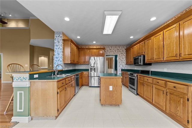 kitchen with a kitchen island, a sink, appliances with stainless steel finishes, brown cabinetry, and wallpapered walls