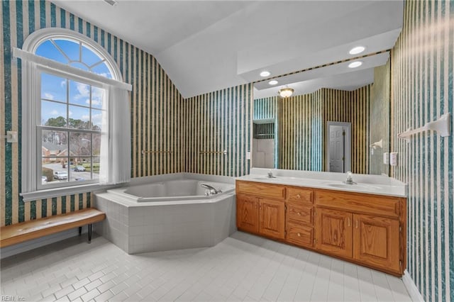 bathroom featuring double vanity, wallpapered walls, vaulted ceiling, a sink, and a bath