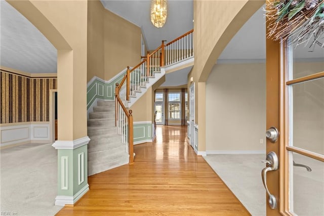 carpeted entryway featuring arched walkways, a decorative wall, a high ceiling, stairs, and crown molding