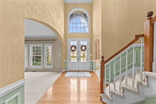 foyer featuring arched walkways, french doors, a wainscoted wall, and stairs