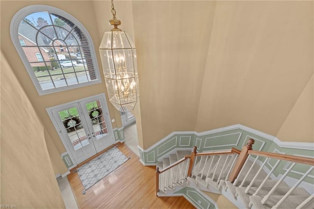 foyer entrance featuring a chandelier, wood finished floors, a towering ceiling, stairs, and french doors