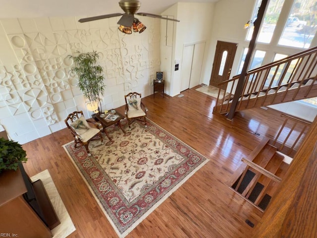 foyer entrance featuring a towering ceiling, ceiling fan, stairs, and wood finished floors