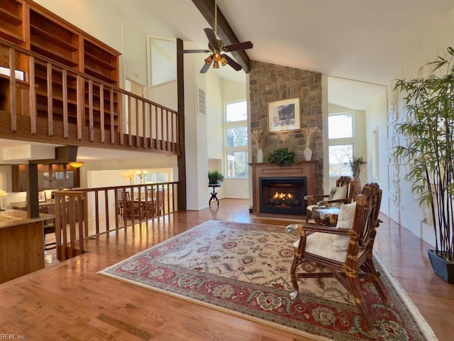 living area with a stone fireplace, plenty of natural light, wood finished floors, and beam ceiling