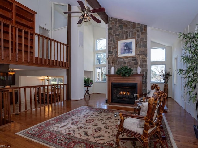 living area with ceiling fan with notable chandelier, high vaulted ceiling, a fireplace, and wood finished floors