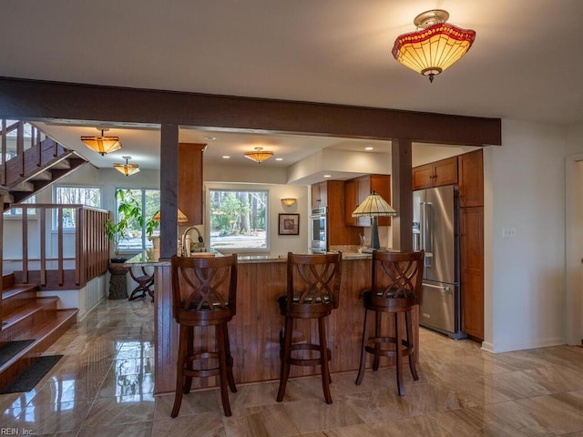 kitchen with appliances with stainless steel finishes, brown cabinetry, a peninsula, and a breakfast bar area