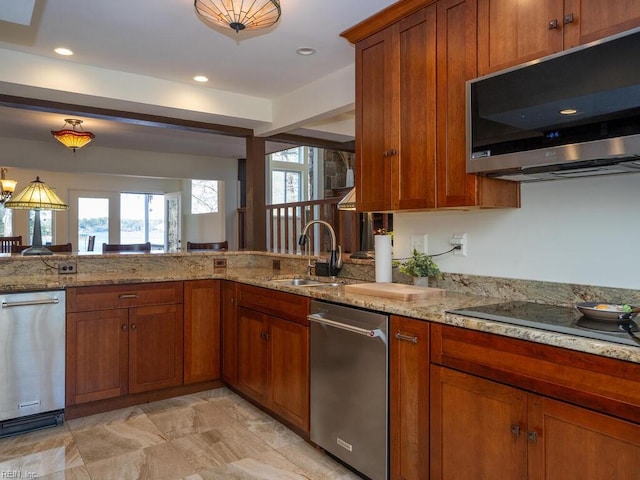 kitchen featuring appliances with stainless steel finishes, brown cabinets, light stone countertops, a sink, and recessed lighting