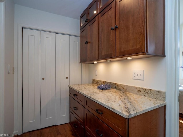 kitchen with light stone counters, brown cabinetry, dark wood finished floors, and glass insert cabinets