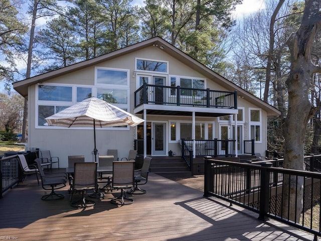 rear view of property with a deck, outdoor dining area, a balcony, and stucco siding