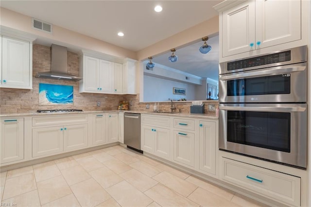 kitchen featuring tasteful backsplash, visible vents, appliances with stainless steel finishes, a sink, and wall chimney range hood